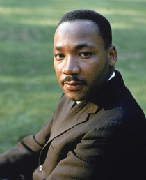 A photo of Dr. Martin Luther King, Jr sitting outside, looking toward the camera
