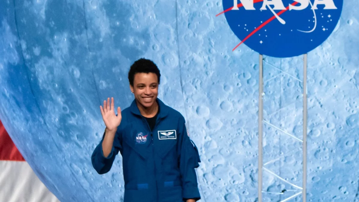 Image of Jessica Watkins, wearing blue NASA uniform, waving and smiling