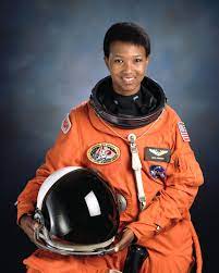 Image of Mae C. Jemison in astronaut gear, holding helmet, smiling at camera