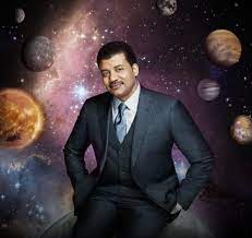Image of Neil deGrasse Tyson, wearing suit and tie, with image of planets in the background