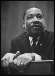 a black and white image of Dr. Martin Luther King, Jr, at a podium.